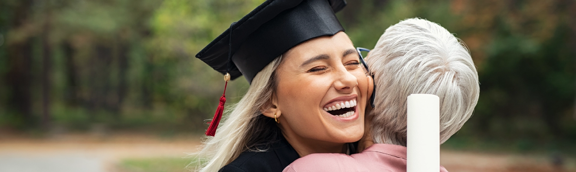 A young graduate with a gown, cap and diploma hugging their parent.